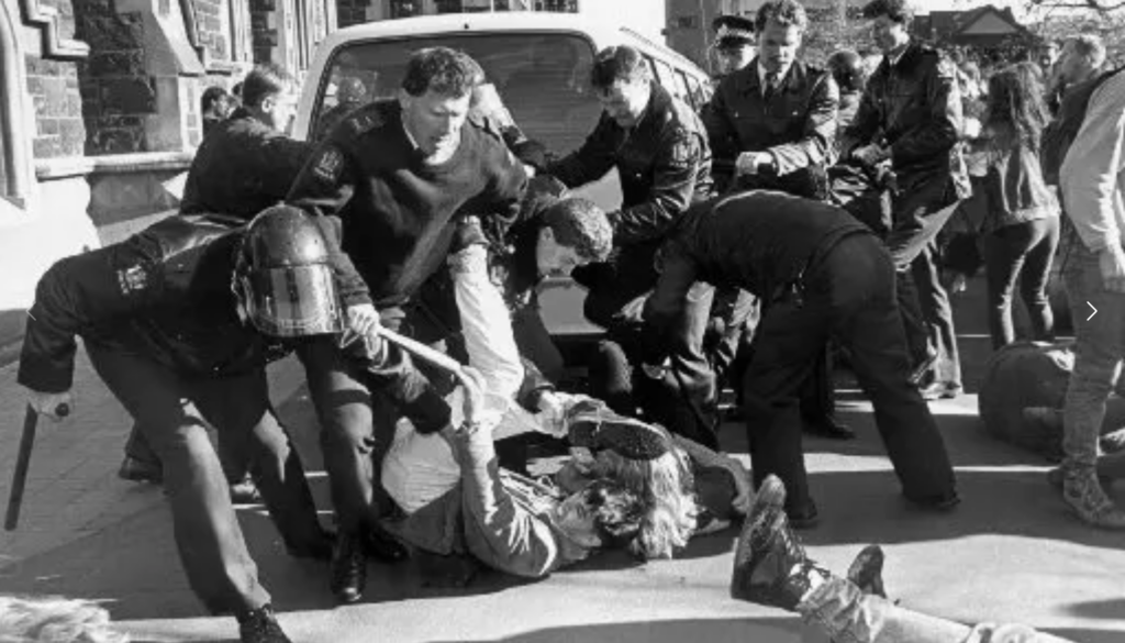 Cops in riot gear beat a student protestor in front of the University of Otago Clocktower building.
Photo Credit: Peter Meecham.